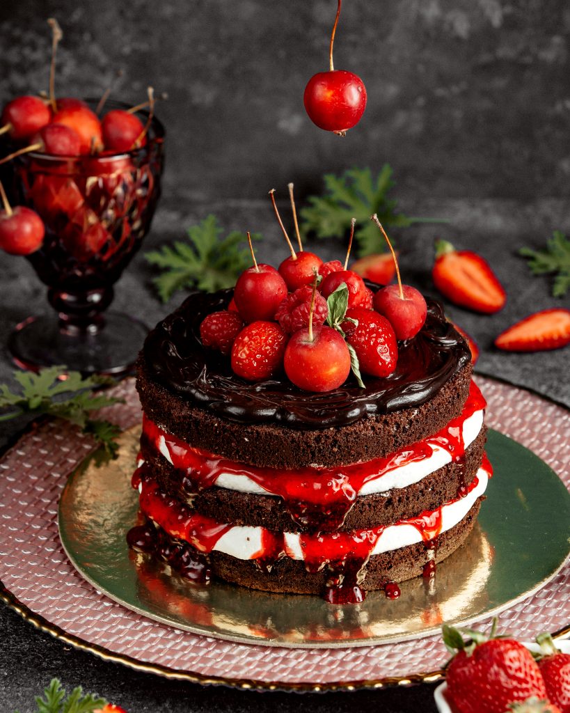 naked chocolate cake decorated with strawberries raspberry small apples and syrup